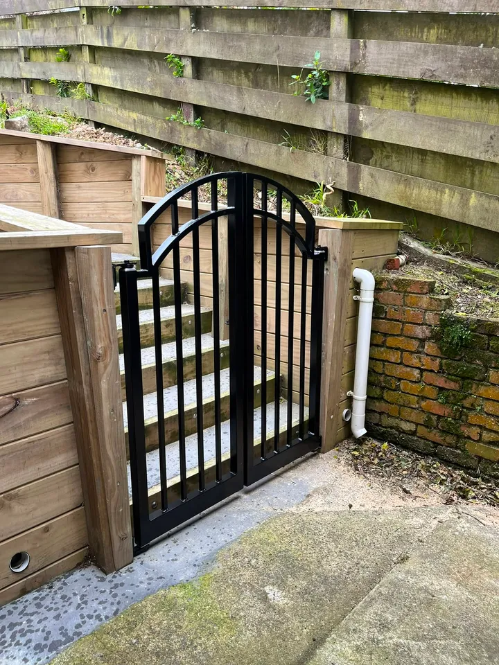 Black steel arched double gate between timber retaining walls
